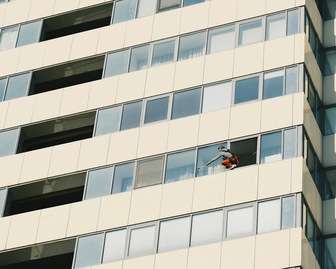 During daylight hours, three window washers hanging from ropes meticulously clean the glass exterior of a contemporary building.